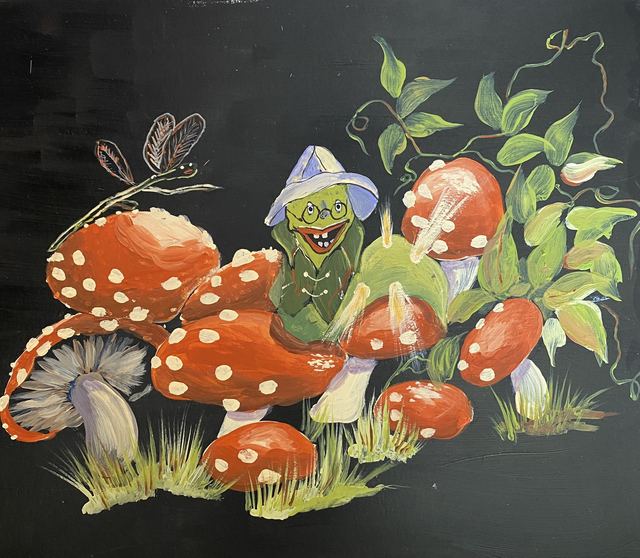 A tiny green fellow in a pale hat peeking out from red spotted mushrooms